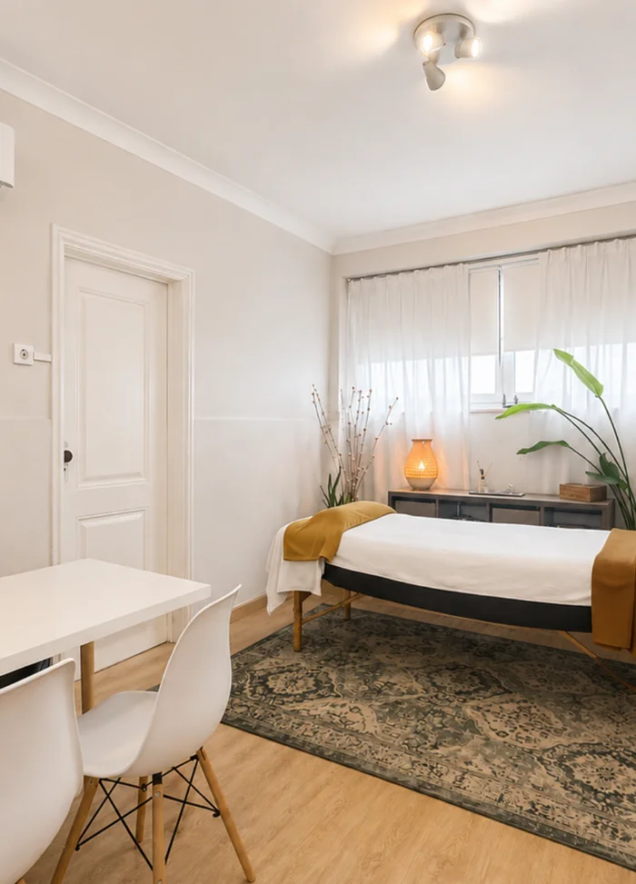 Sala de atendimento luminosa, com marquesa, tapete e mesa