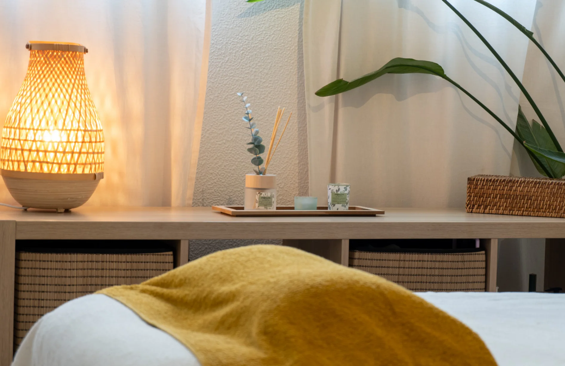 Marquesa com manta mostarda, candeeiro de luz quente e plantas no espaço de atendimento